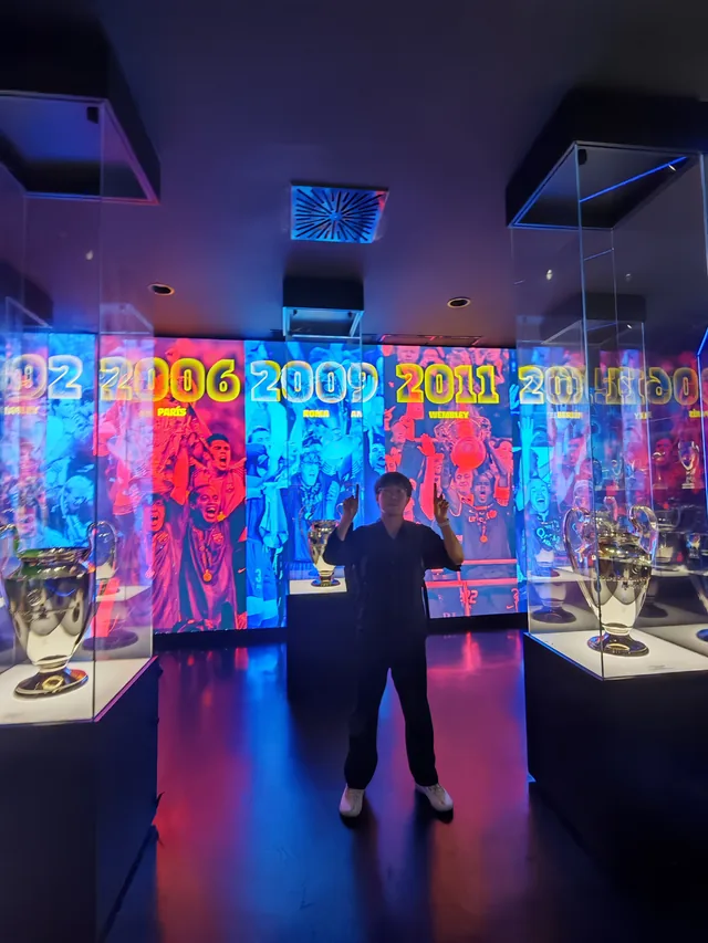 Huiyao standing between trophy displays in the FC Barcelona exhibition