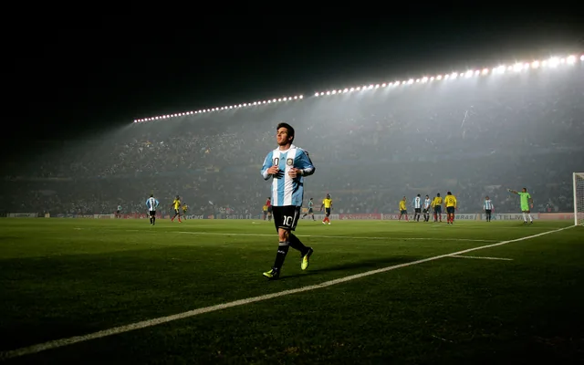 Lionel Messi on a floodlit pitch, with the stands behind him